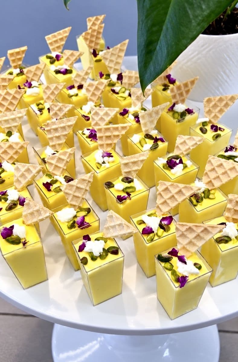 Yellow dessert cups with wafers and colorful toppings on a round catering platter
